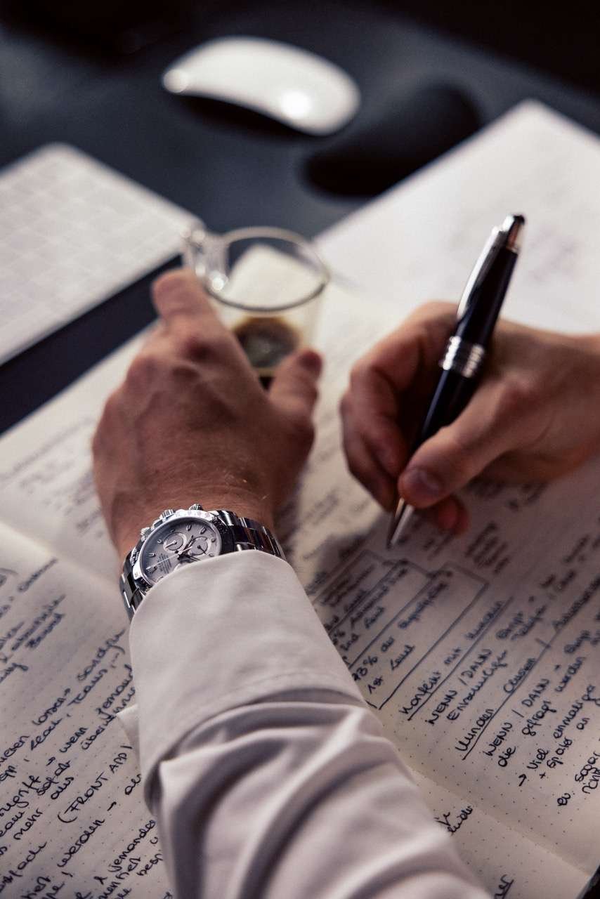 Nahaufnahme von Sebastian Klein's Hand, die eine Branding-Strategie in ein Notizbuch skizziert, mit einer Rolex Uhr und einem Mont Blanc Stift